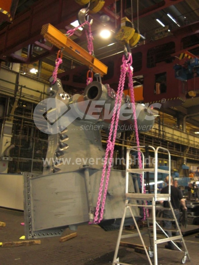 Ein Maschinenbauteil wird mit vier Kranzketten, an zwei Kranen per Aufhängering und Lasttraverse verbunden, in einer Halle gehoben