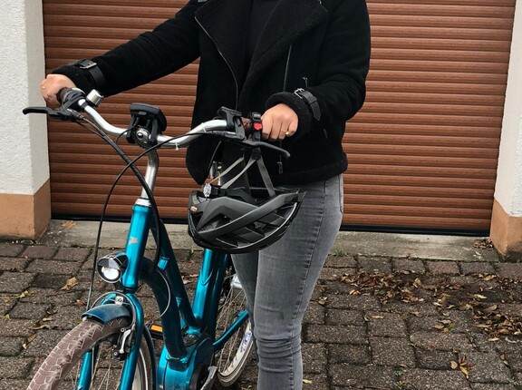 Eine Mitarbeiterin der Evers GmbH steht neben ihrem blauen Fahrrad vor einer Garage