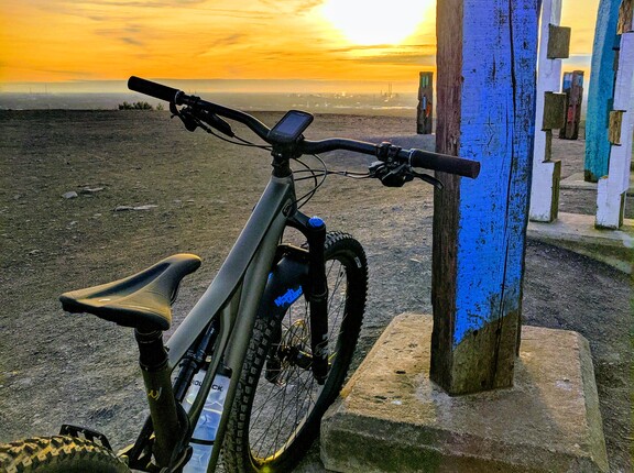 Ein E-Bike, angelehnt an einen blauen Pfahl, mit dem Sonnenuntergang im Hintergrund