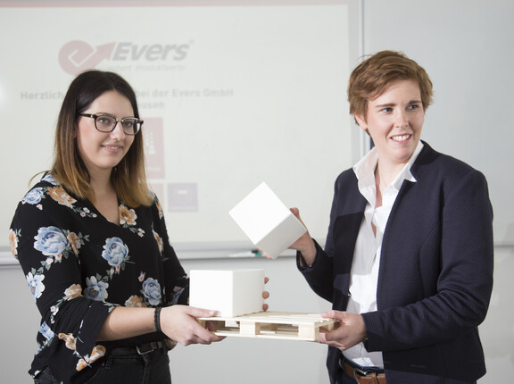 Zwei Mitarbeiter der Evers GmbH zeigen konforme Palettensicherung anhand einer Miniatur-Palette